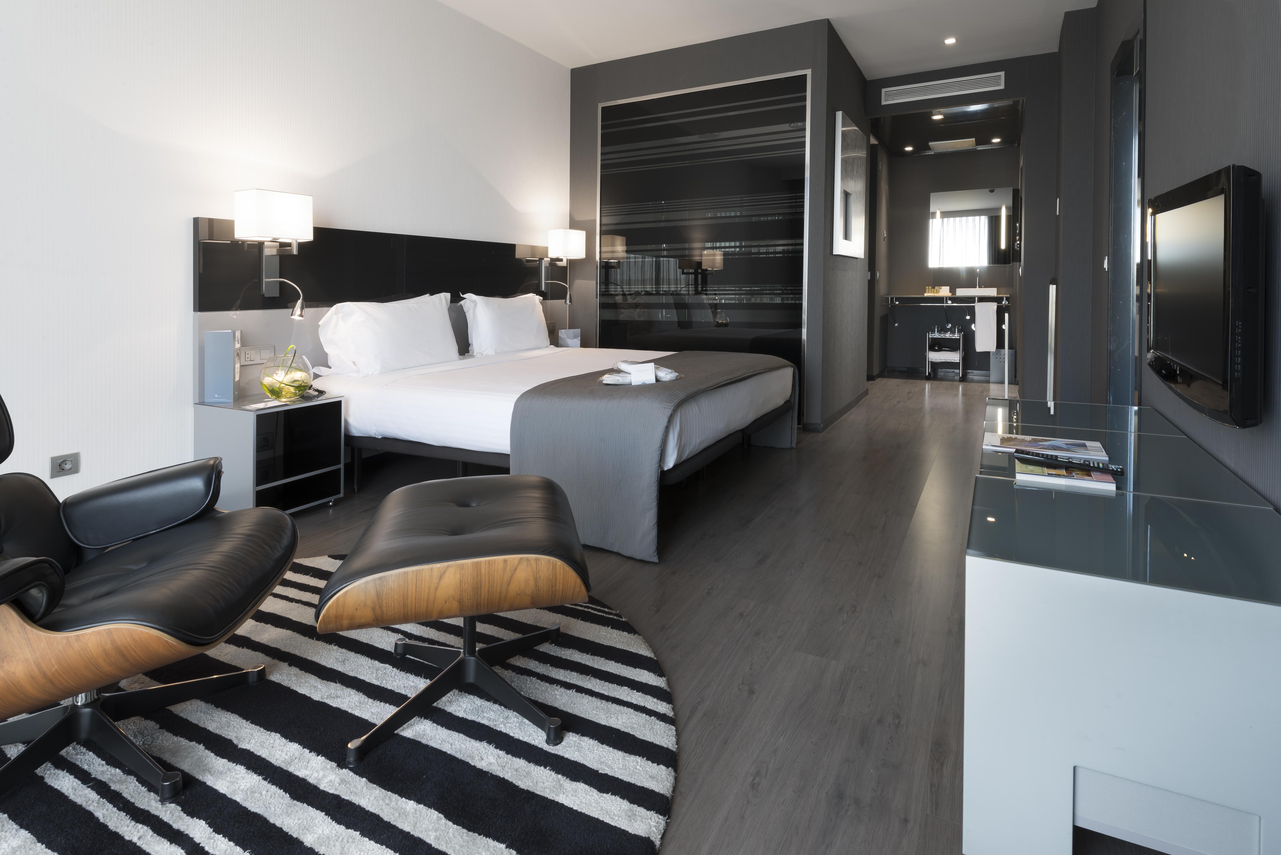 ยูโรสตาร์ส พาเลซ โฮเต็ล Hotel กอร์โดบา ภายนอก รูปภาพ The photo shows a modern hotel room featuring a king-sized bed with light-colored linens and dark accent walls. There are stylish bedside tables with lamps, and a comfortable lounge chair paired with an ottoman placed on a striped rug. The room also 
