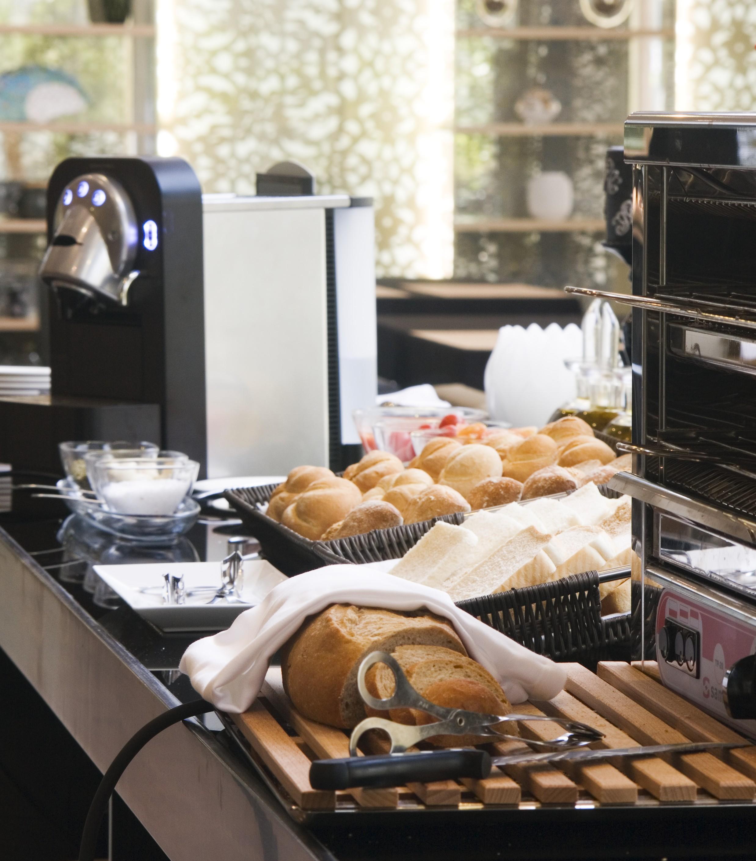 ยูโรสตาร์ส พาเลซ โฮเต็ล Hotel กอร์โดบา ภายนอก รูปภาพ The photo shows a dining setup featuring various food items. On the left, there is a coffee machine, and in the foreground, there is a basket of freshly baked bread rolls. Next to the rolls, there are slices of bread arranged neatly. In the backgroun