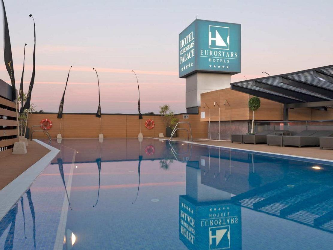 ยูโรสตาร์ส พาเลซ โฮเต็ล Hotel กอร์โดบา ภายนอก รูปภาพ The image shows a hotel pool area at twilight. The pool is large and reflective, capturing the colors of the sky and surrounding features. In the background, there is a hotel sign displaying the Eurostars brand, with a modern architecture style. The 