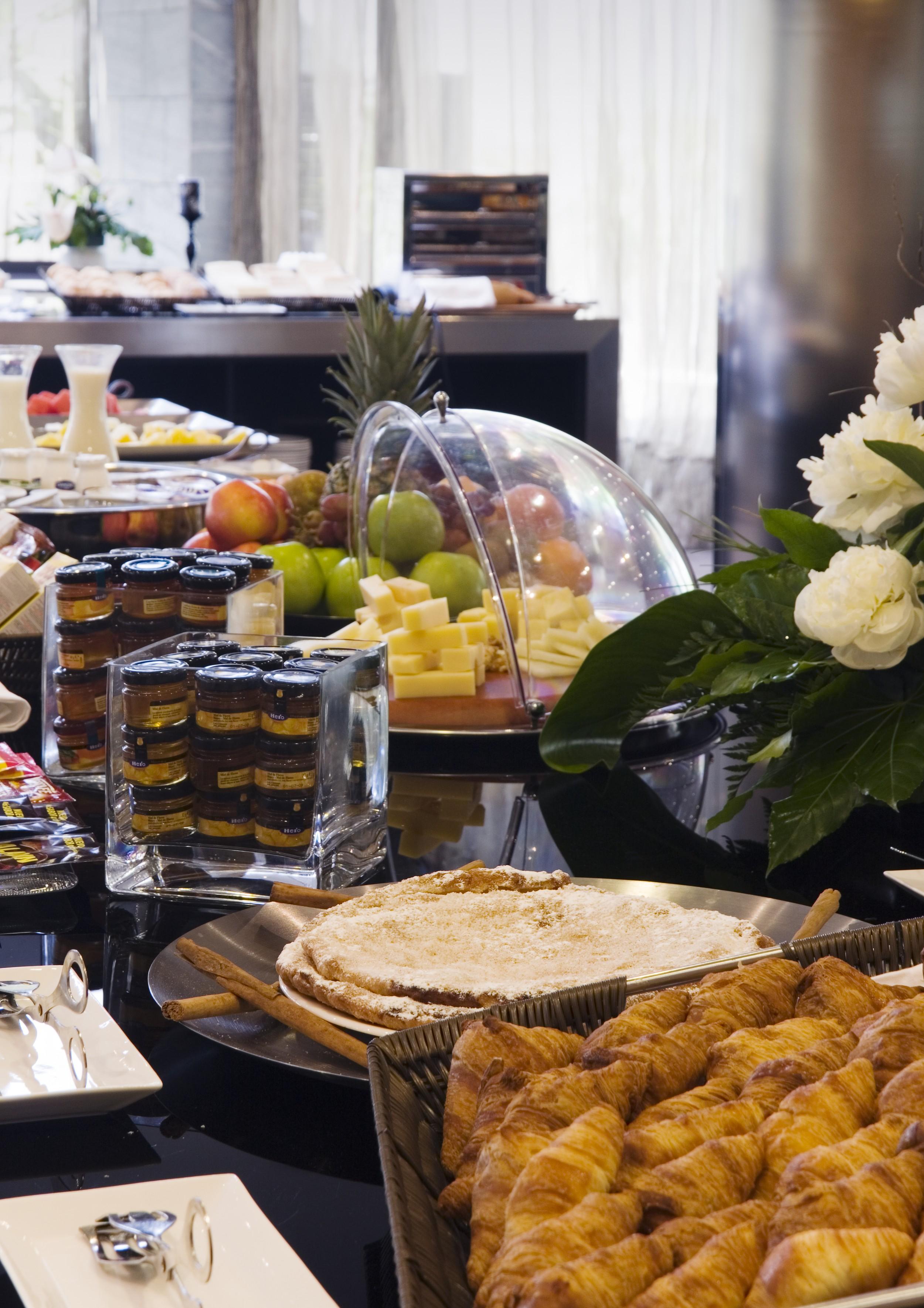 ยูโรสตาร์ส พาเลซ โฮเต็ล Hotel กอร์โดบา ภายนอก รูปภาพ The photo shows a buffet-style arrangement with a variety of food items. There are fruits such as apples and grapes displayed prominently, along with a selection of cheeses presented on a wooden platter. A glass dome covers some of the items, possibl