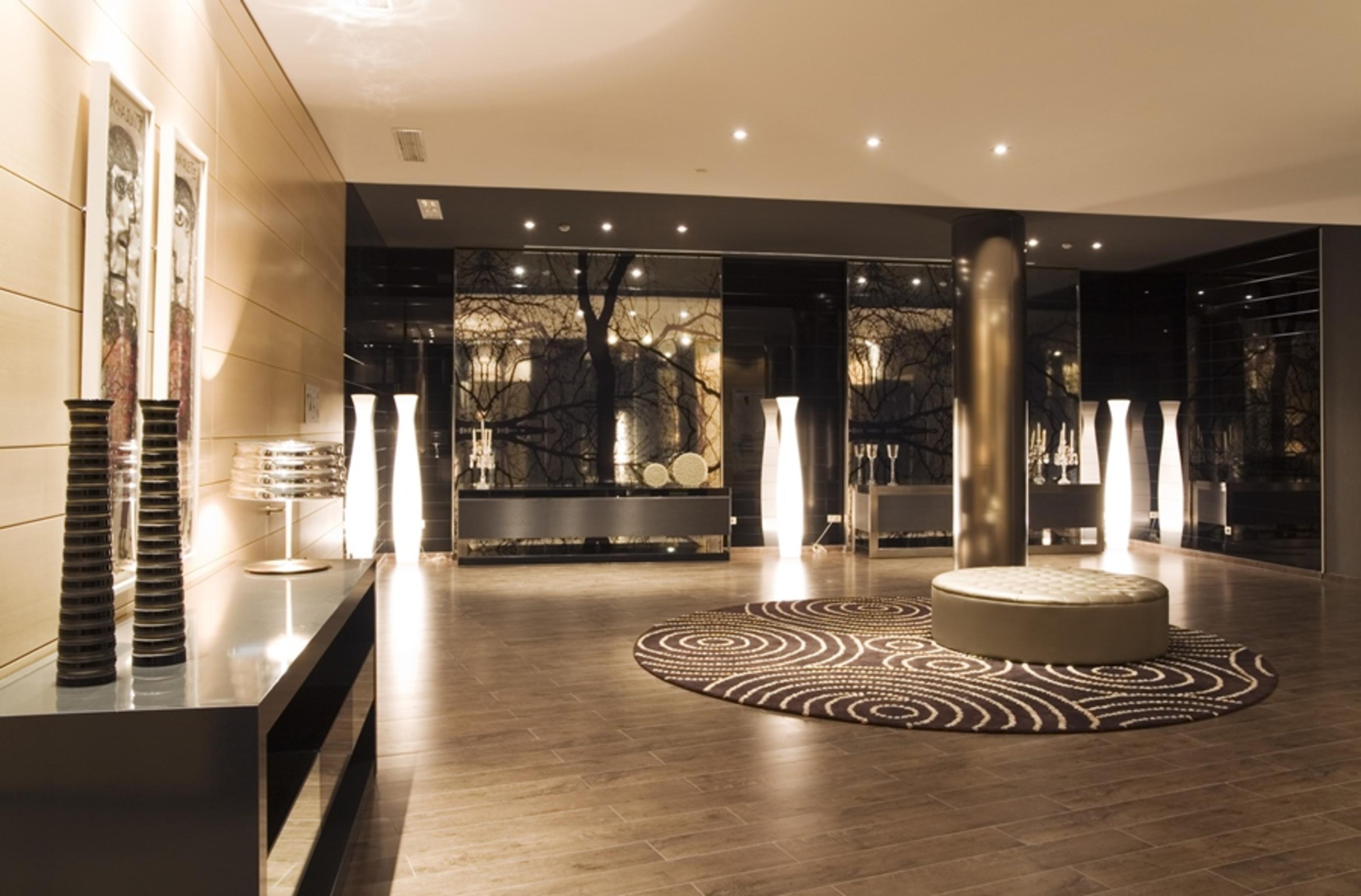 ยูโรสตาร์ส พาเลซ โฮเต็ล Hotel กอร์โดบา ภายนอก รูปภาพ The photo shows a modern interior space, likely a lobby or waiting area. The design features polished wooden flooring and sleek surfaces. There are tall, artistic light fixtures scattered throughout, contributing to a sophisticated ambiance. A round 