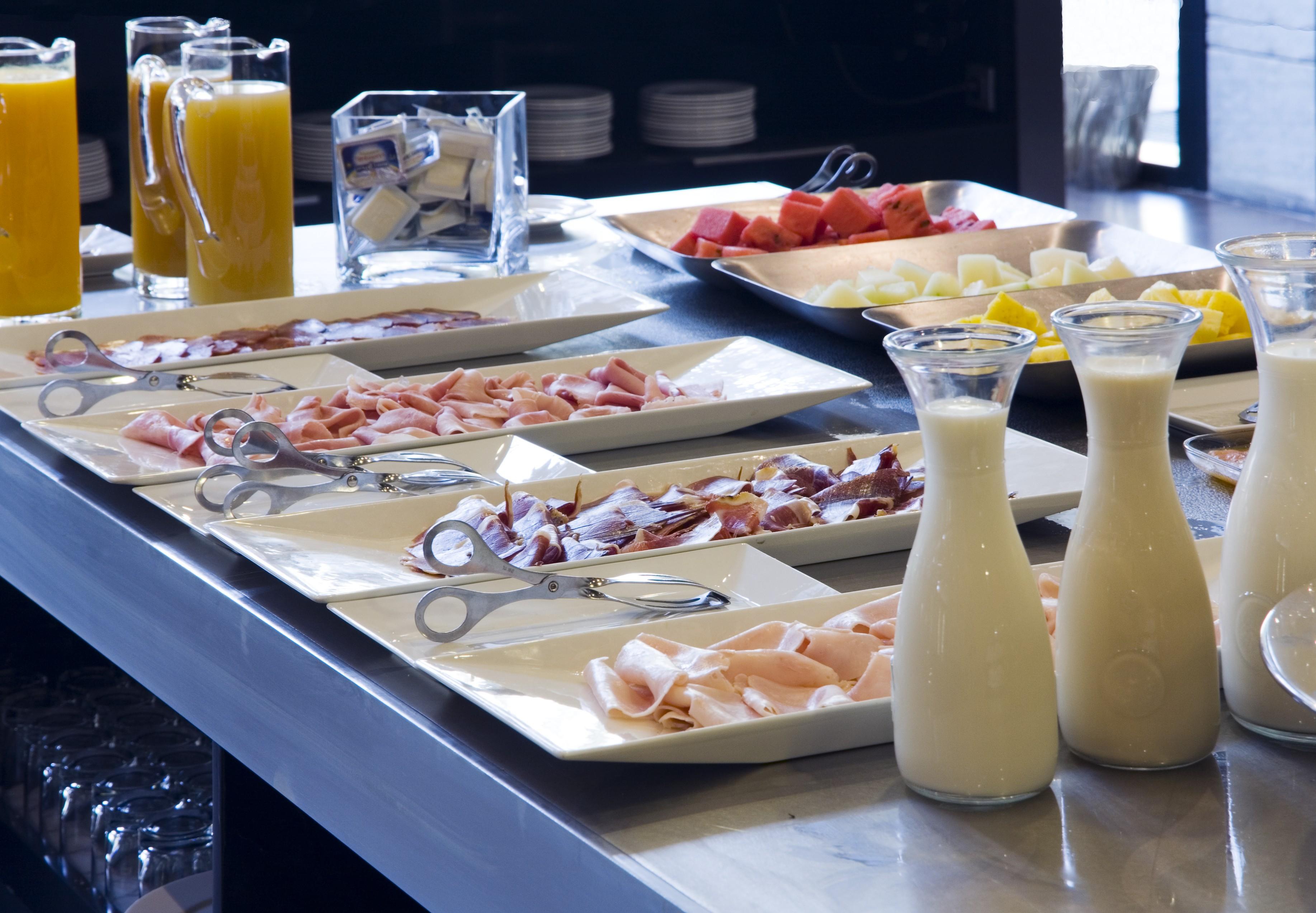 ยูโรสตาร์ส พาเลซ โฮเต็ล Hotel กอร์โดบา ภายนอก รูปภาพ The photo displays a buffet area with various food items arranged on a countertop. There are multiple plates featuring an assortment of sliced meats, likely including ham and possibly turkey or chicken. Additionally, two glass pitchers are filled wit
