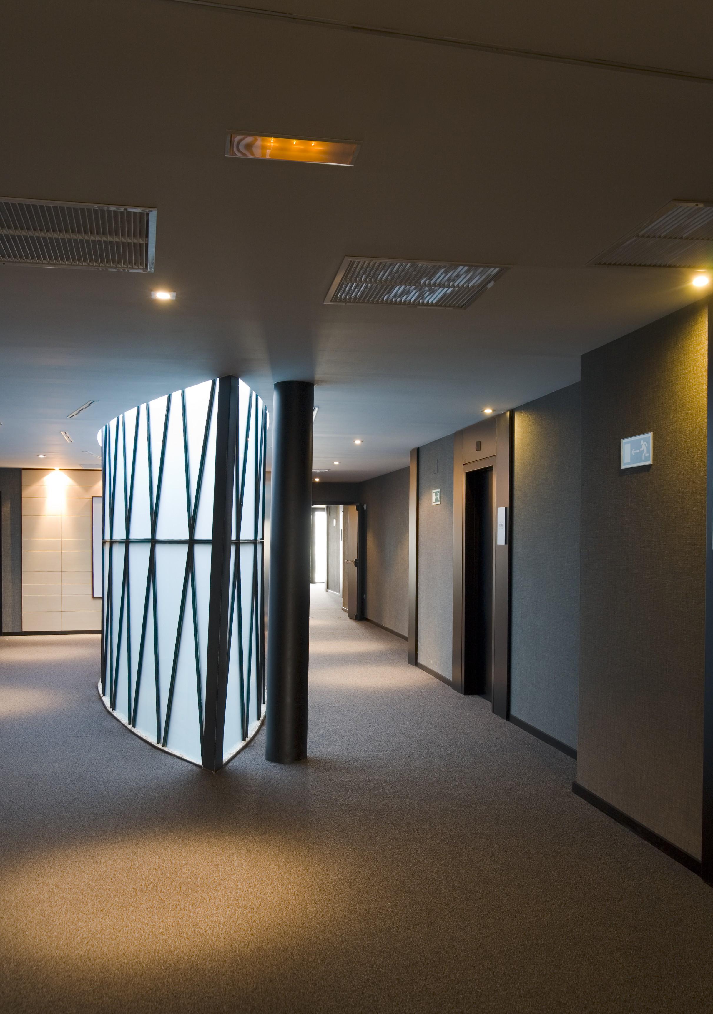 ยูโรสตาร์ส พาเลซ โฮเต็ล Hotel กอร์โดบา ภายนอก รูปภาพ The photo shows a modern indoor corridor featuring a smooth, curved wall with a geometric pattern. The corridor is well-lit with recessed ceiling lights, and the floor is carpeted. There are doors leading to elevators on the right side, and the walls