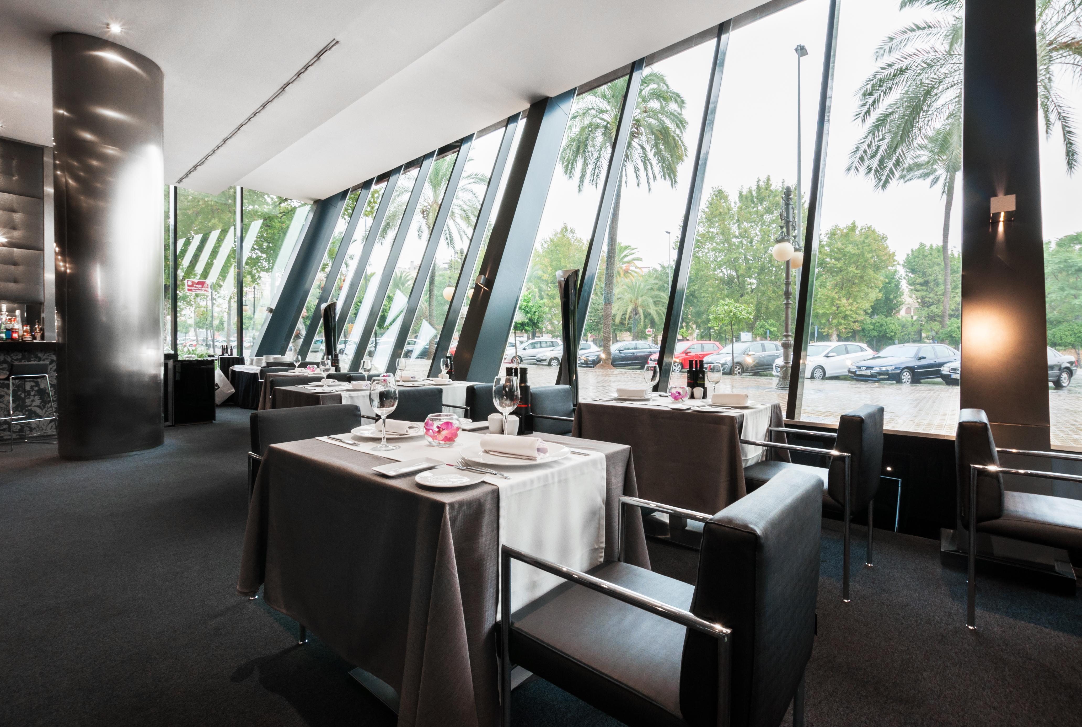 ยูโรสตาร์ส พาเลซ โฮเต็ล Hotel กอร์โดบา ภายนอก รูปภาพ The photo shows the interior of a modern restaurant featuring large glass windows that provide an expansive view of the outdoors, including palm trees. The dining area is elegantly set up with tables covered in gray tablecloths, decorated with simple