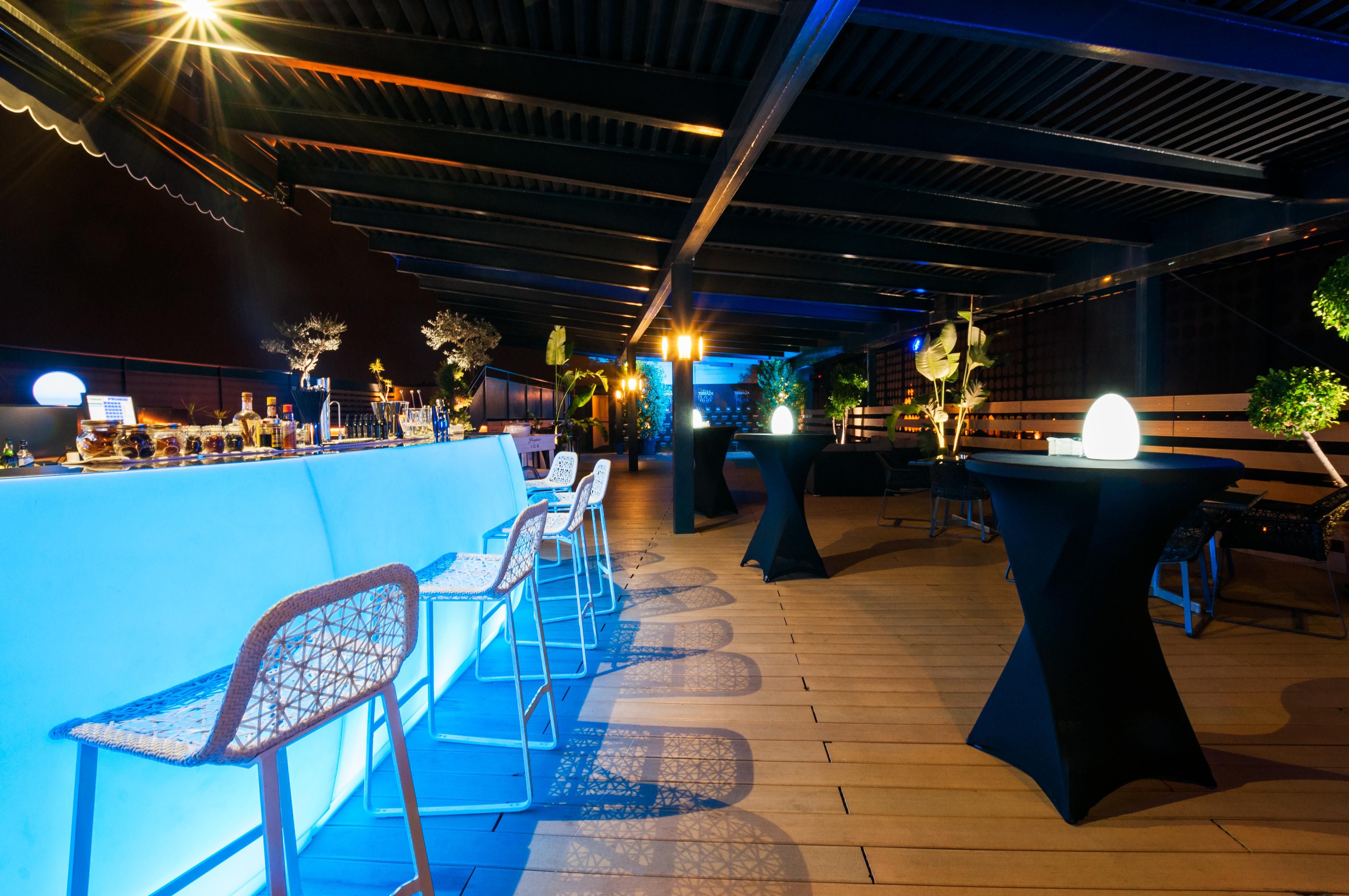 ยูโรสตาร์ส พาเลซ โฮเต็ล Hotel กอร์โดบา ภายนอก รูปภาพ The photo shows a stylish rooftop or outdoor bar area. There is a long bar counter illuminated with blue lighting, complemented by modern bar stools. The space is decorated with potted plants and elegant round tables covered in black cloth. Soft ligh