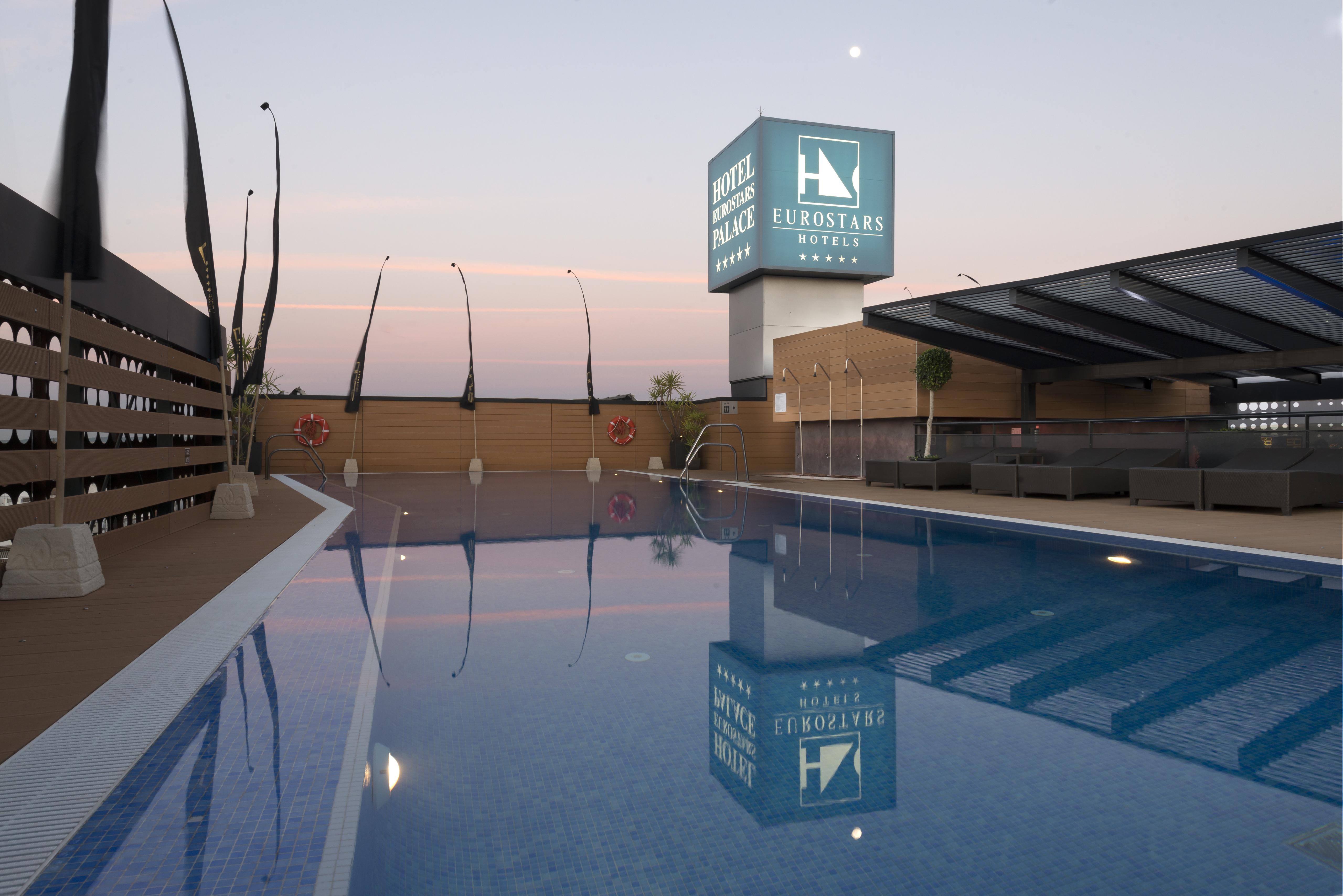 ยูโรสตาร์ส พาเลซ โฮเต็ล Hotel กอร์โดบา ภายนอก รูปภาพ The photo shows a rooftop space featuring a swimming pool. The pool has a clear blue water, and the area around it is designed with modern aesthetics, including a wooden deck and comfortable seating. In the background, there is a prominent sign for "