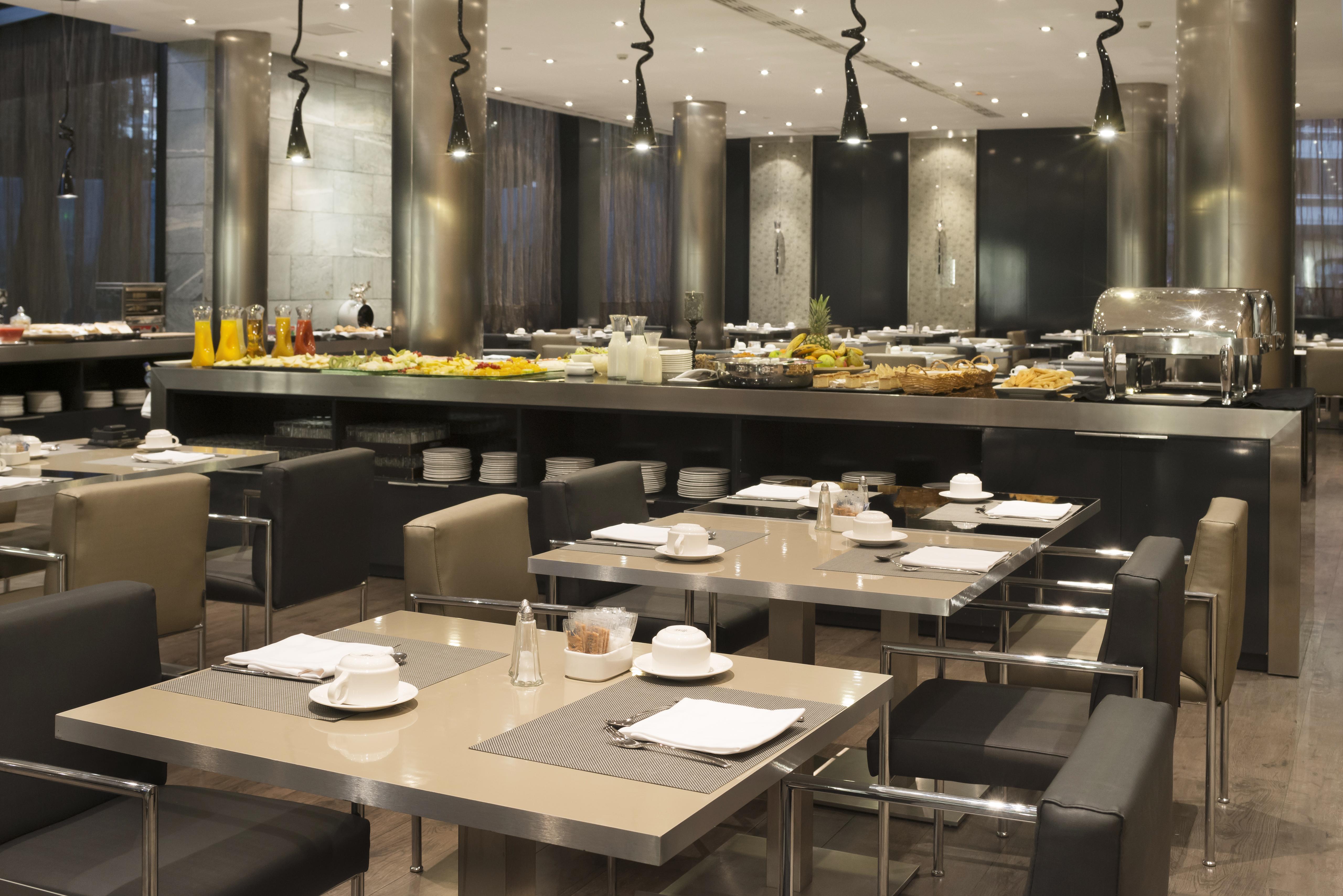ยูโรสตาร์ส พาเลซ โฮเต็ล Hotel กอร์โดบา ภายนอก รูปภาพ The photo depicts a modern restaurant interior featuring a spacious dining area with several tables. Each table is set with plates and cutlery, suggesting it's prepared for guests. In the background, there is a buffet station with an extensive displa