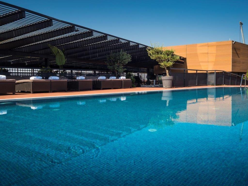 ยูโรสตาร์ส พาเลซ โฮเต็ล Hotel กอร์โดบา ภายนอก รูปภาพ The photo shows a rooftop swimming pool with a clear, vibrant blue surface reflecting the sky. Surrounding the pool are comfortable lounge chairs, some shaded by a modern overhead structure. The area is accented with potted plants, adding greenery to