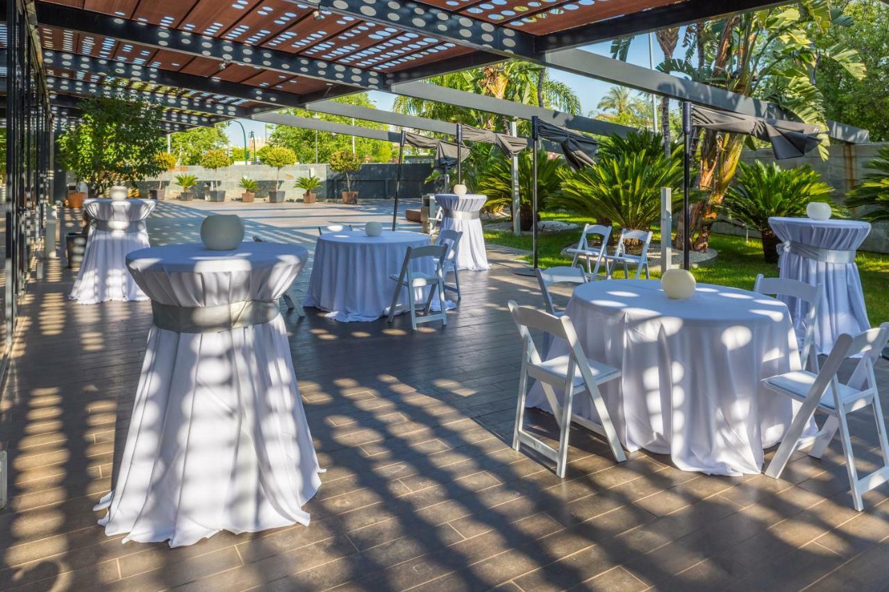 ยูโรสตาร์ส พาเลซ โฮเต็ล Hotel กอร์โดบา ภายนอก รูปภาพ The photo shows an outdoor event setup. There are several round tables covered with white tablecloths, some adorned with decorative elements like small centerpieces. Chairs are arranged around the tables, and the area is surrounded by greenery, inclu